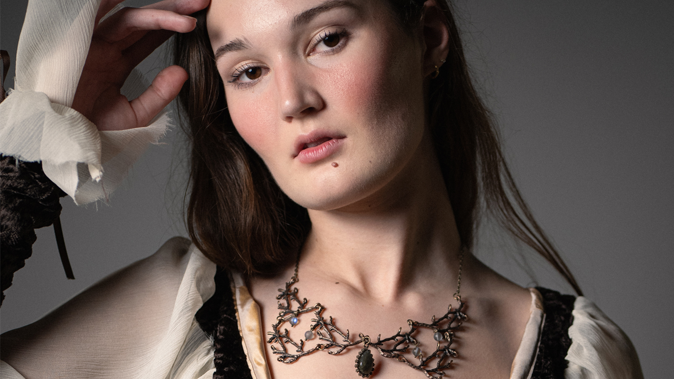 Editorial portrait of model wearing cream blouse and statement necklace in studio lighting